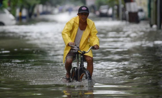 菲律宾暴雨，马尼拉洪涝灾害，一名骑自行车的男子涉水穿过被洪水淹没的街道。